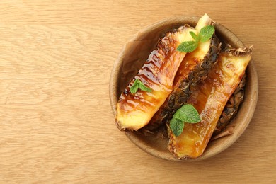 Photo of Tasty grilled pineapples in bowl on wooden table, top view. Space for text