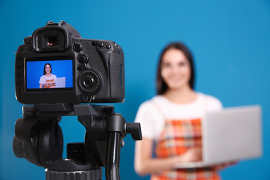 Young blogger with laptop recording video against blue background, focus on camera screen