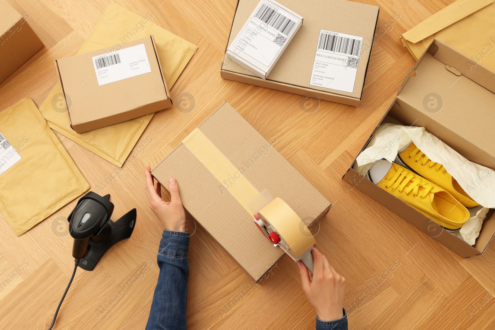 Photo of Woman taping parcel at wooden table in office, top view. Online store