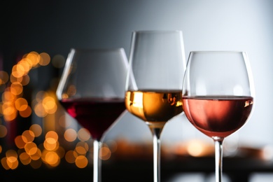 Photo of Glasses with different wines against defocused lights, closeup. Space for text