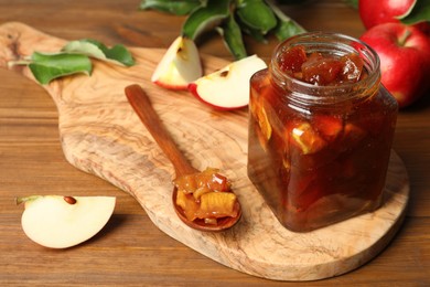 Photo of Tasty apple jam in glass jar and fresh fruits on wooden table, space for text