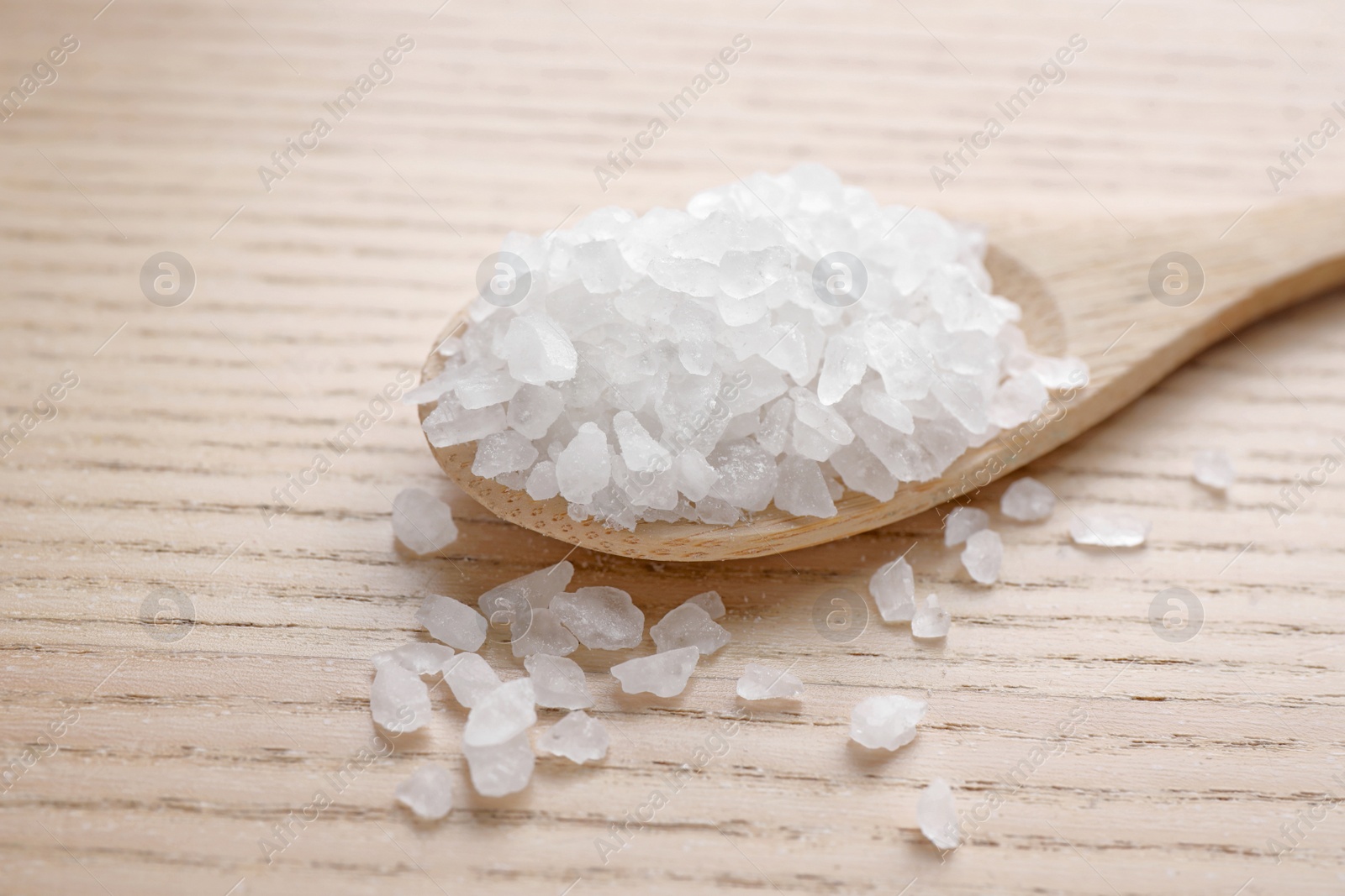 Photo of Spoon with white sea salt on wooden table, closeup. Spa treatment