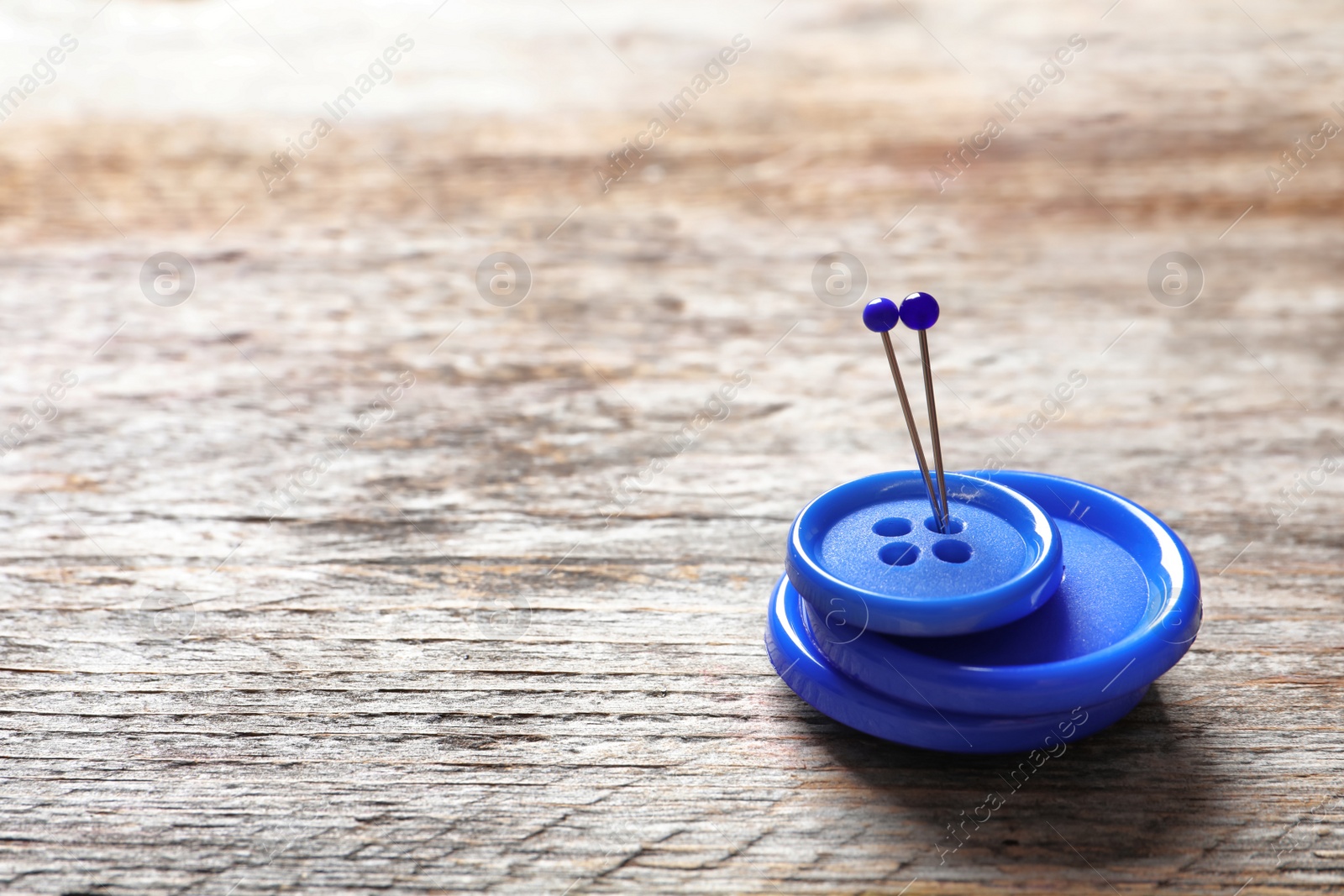 Photo of Blue buttons with pins on wooden background. Tailoring equipment