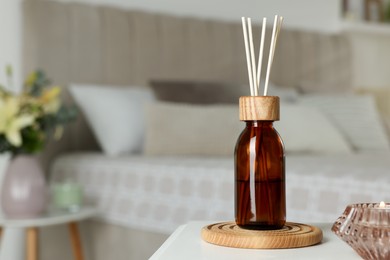 Photo of Aromatic reed air freshener and candle on white table in bedroom. Space for text