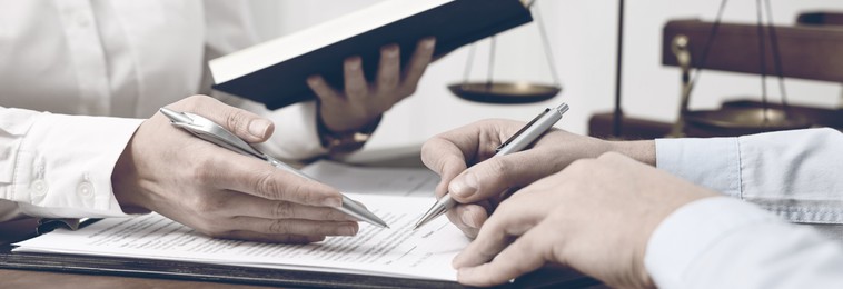 Lawyer pointing at document and client putting signature at table in office, closeup. Banner design