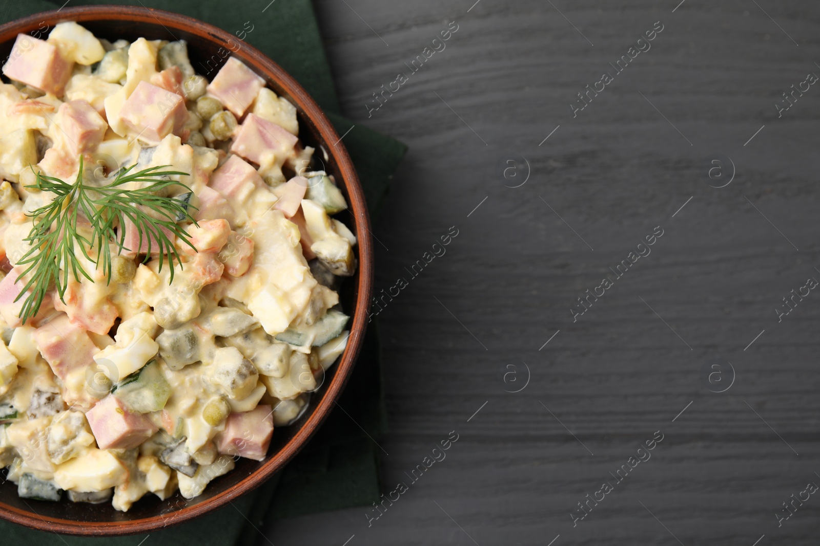 Photo of Tasty Olivier salad with boiled sausage in bowl on grey wooden table, top view. Space for text
