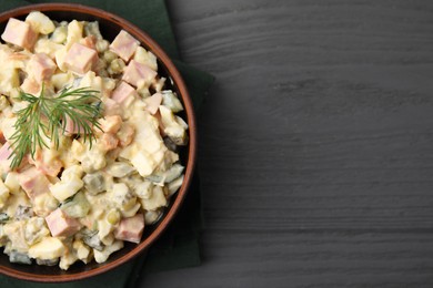 Tasty Olivier salad with boiled sausage in bowl on grey wooden table, top view. Space for text