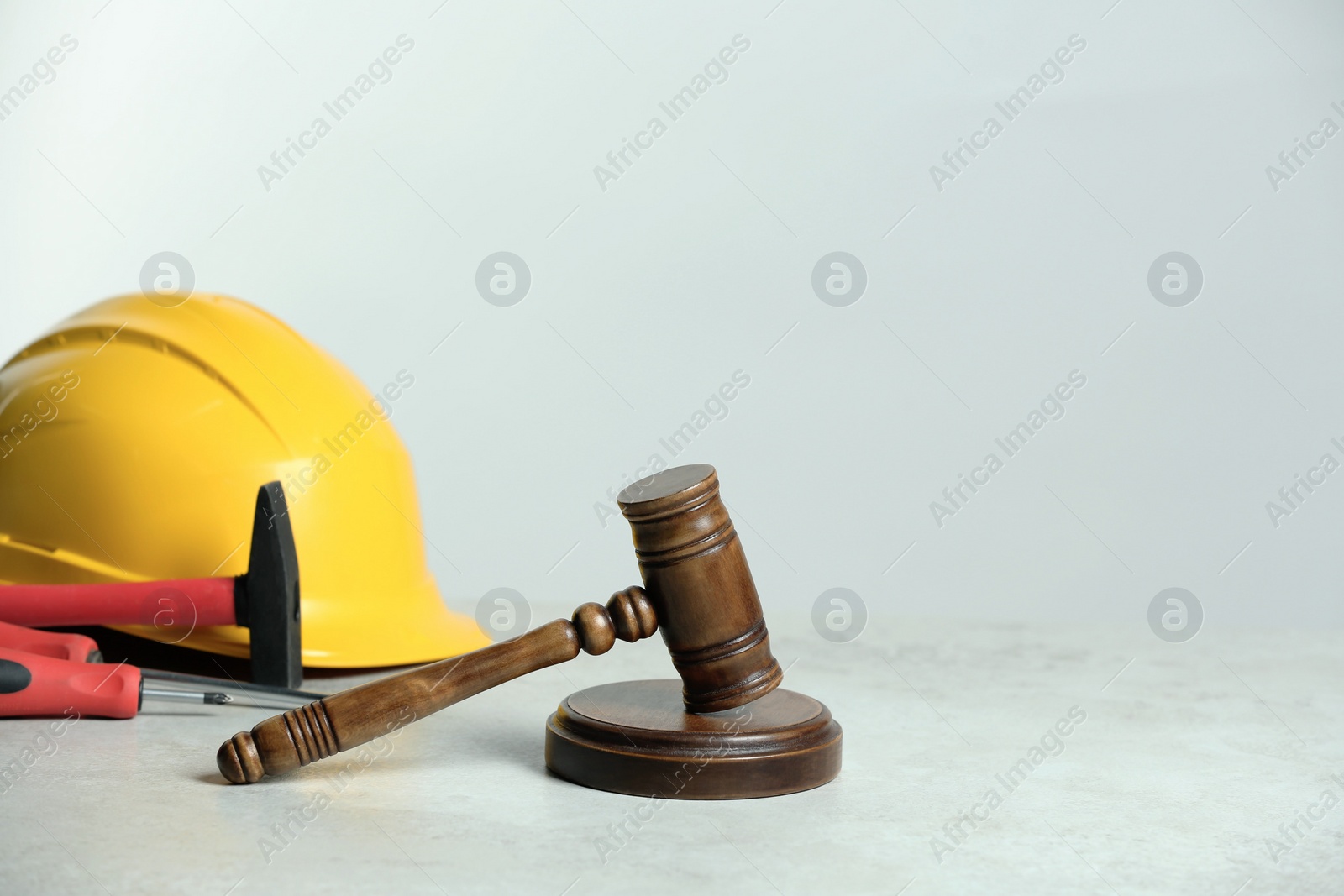Photo of Construction and land law concepts. Gavel, hard hat, hammer and screwdrivers on white table, space for text