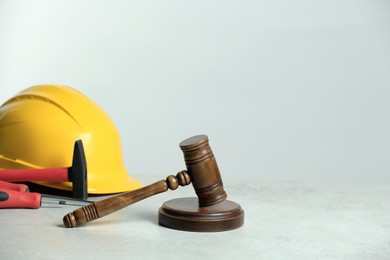 Photo of Construction and land law concepts. Gavel, hard hat, hammer and screwdrivers on white table, space for text