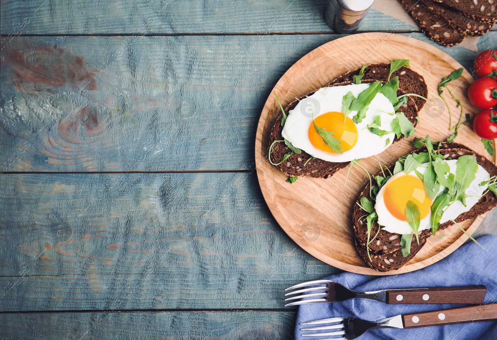 Photo of Delicious sandwiches with arugula and fried egg on blue wooden table, flat lay. Space for text