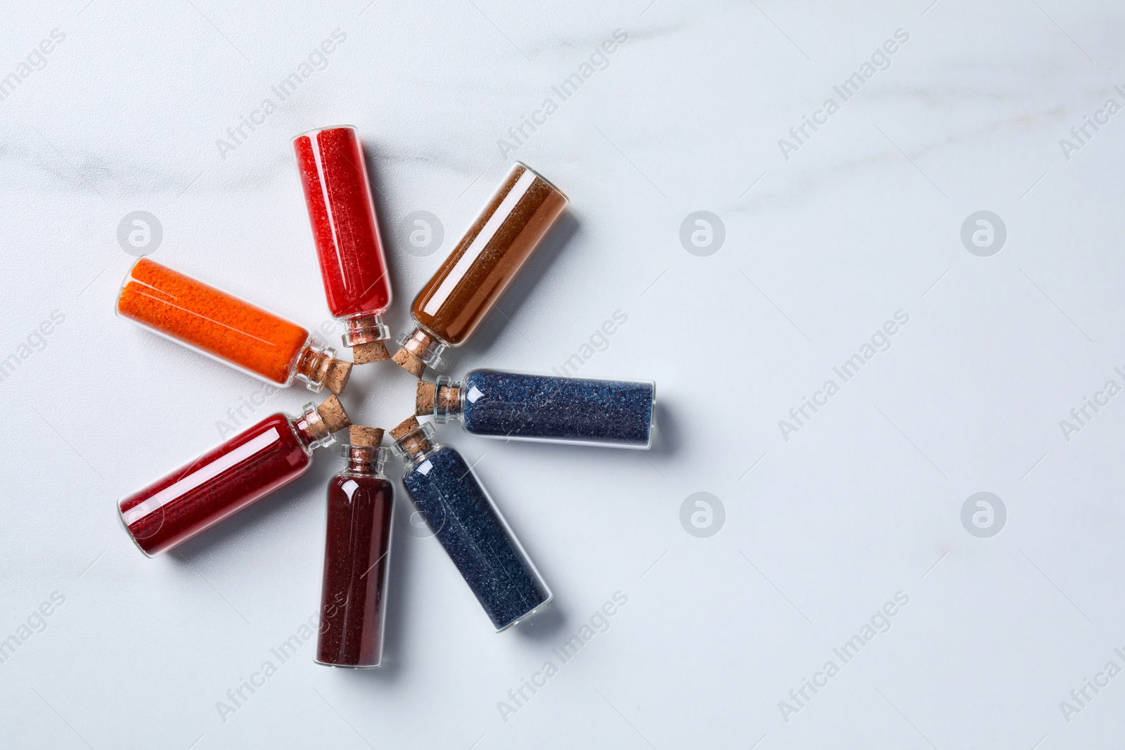 Photo of Glass bottles with different food coloring on white marble table, flat lay. Space for text