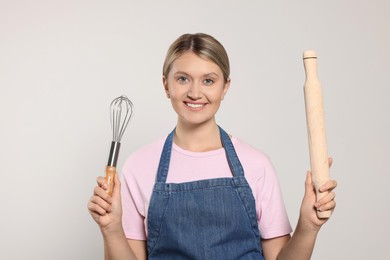 Photo of Beautiful young woman in clean apron with kitchen tools on light grey background