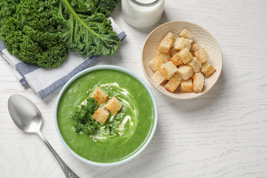 Tasty kale soup served on white wooden table, flat lay