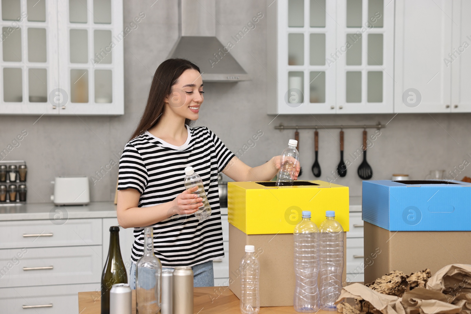 Photo of Smiling woman separating garbage at table in kitchen
