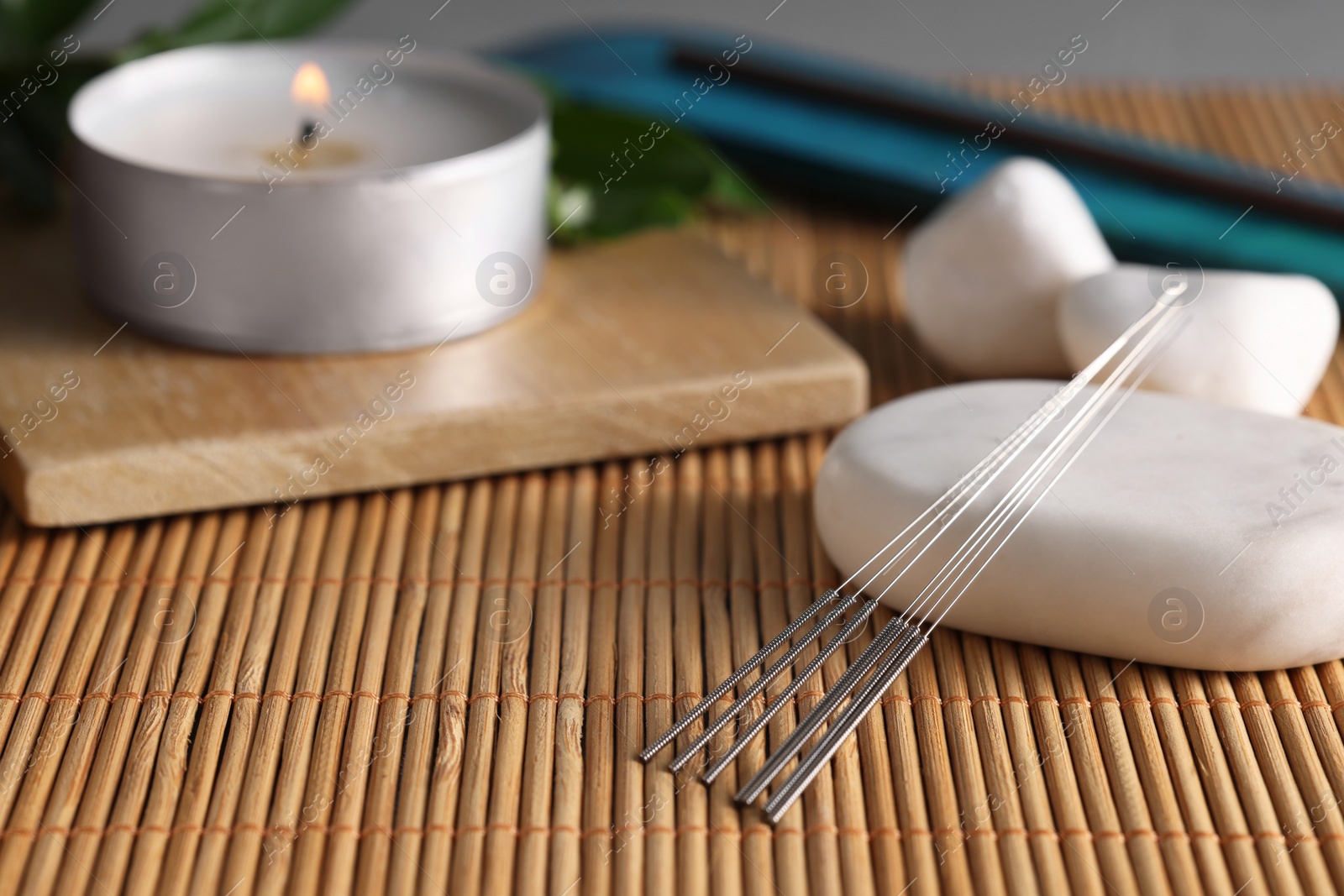 Photo of Acupuncture needles, spa stones and burning candle on bamboo mat. Space for text