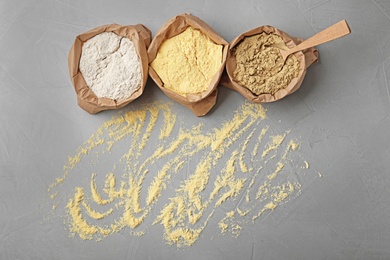 Photo of Paper bags with different types of flour on gray background