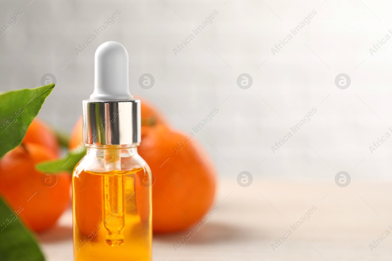 Photo of Bottle of tangerine essential oil and fresh fruits on light background, closeup. Space for text