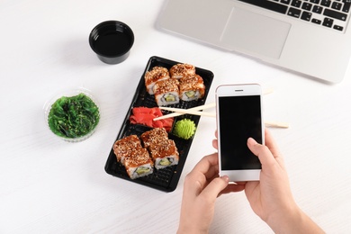 Woman with mobile phone and sushi rolls at table, space for text. Food delivery