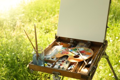 Photo of Easel with blank canvas and painting equipment in countryside