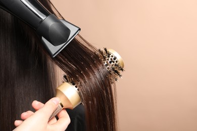 Hairdresser blow drying client's hair on beige background, closeup. Space for text
