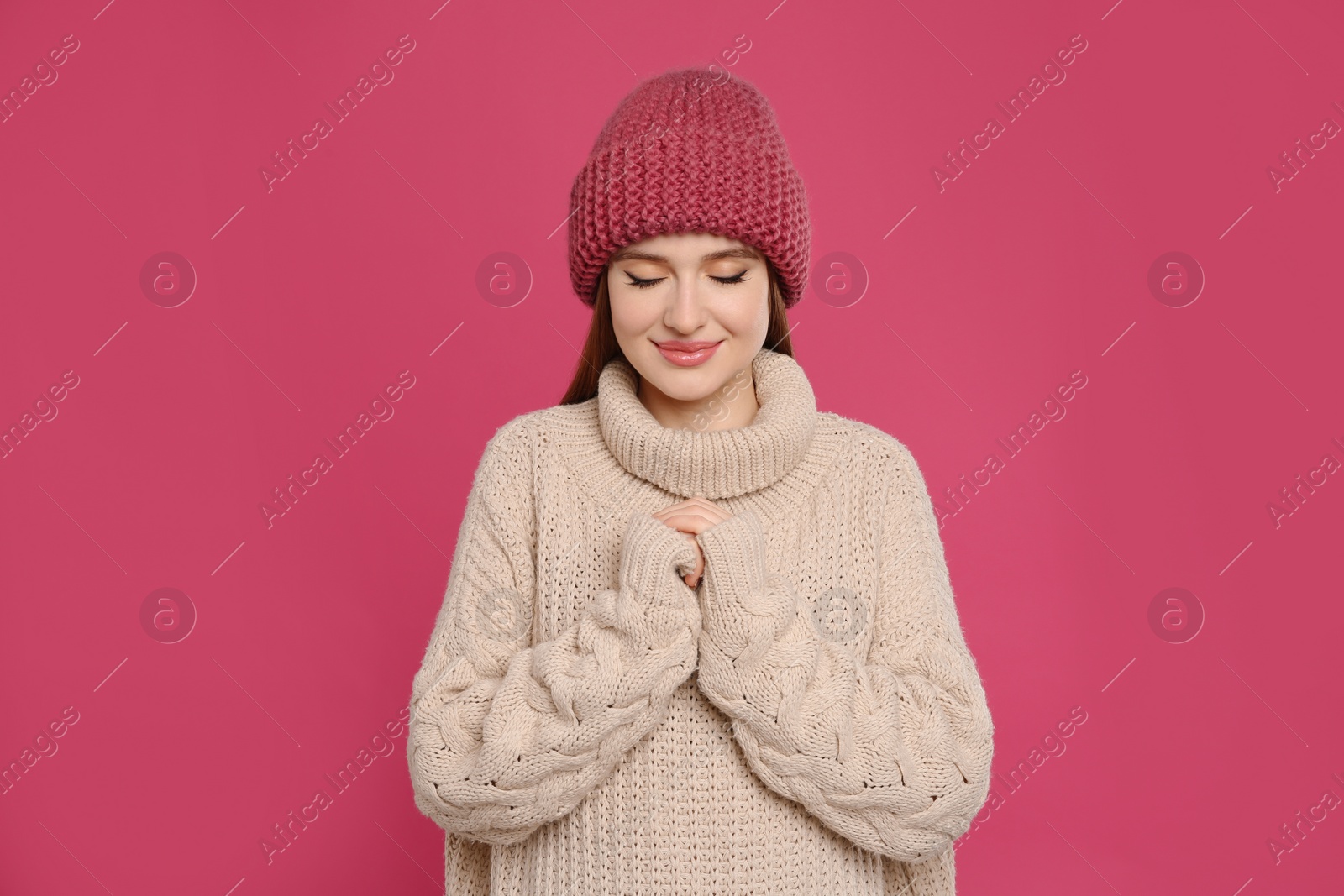 Photo of Young woman wearing warm sweater and hat on crimson background. Winter season