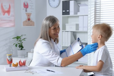 Endocrinologist examining boy's thyroid gland at table in hospital