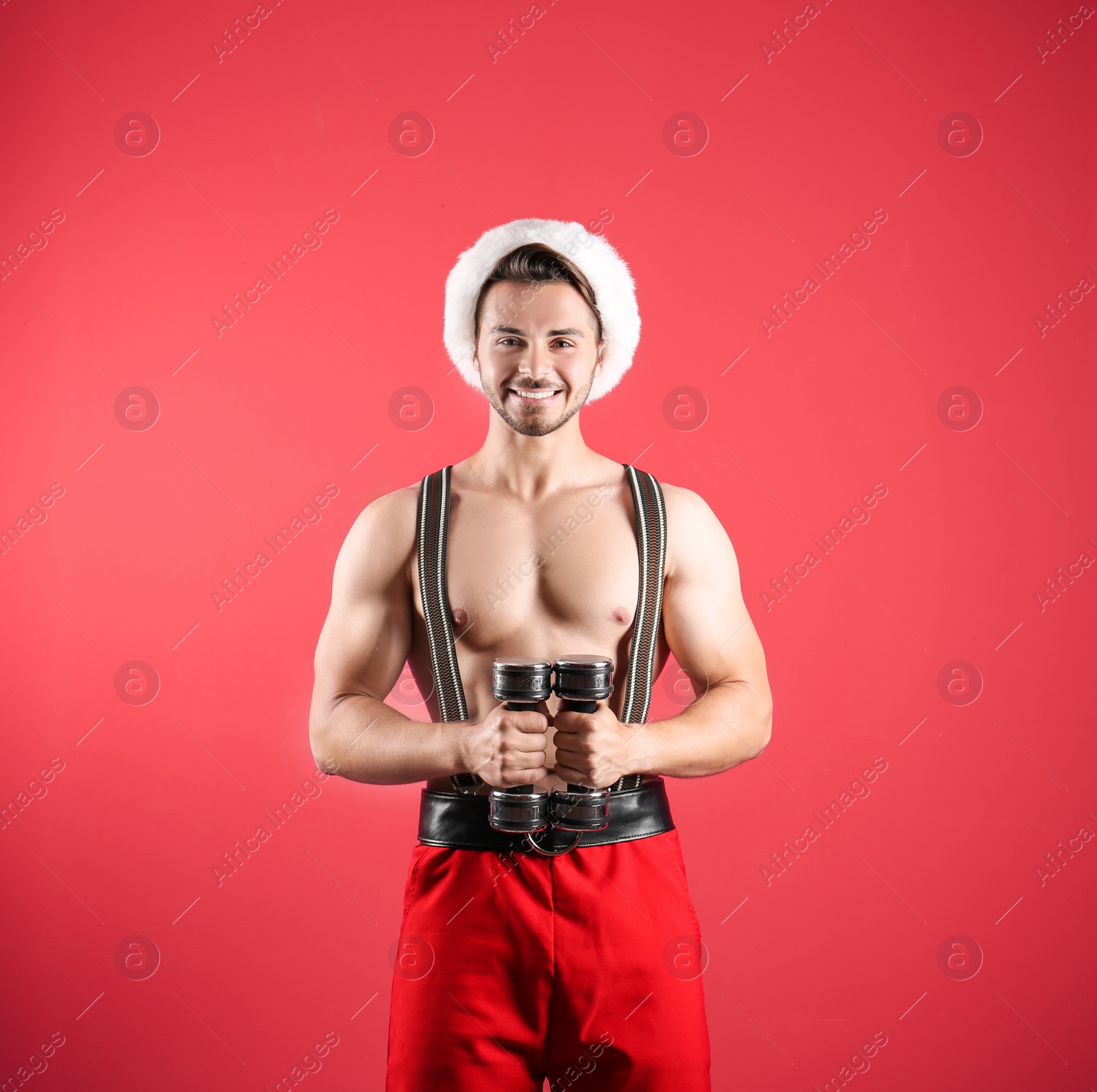 Photo of Shirtless sexy young Santa Claus with dumbbells on color background