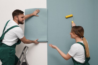 Photo of Workers hanging stylish wall paper sheet on light background