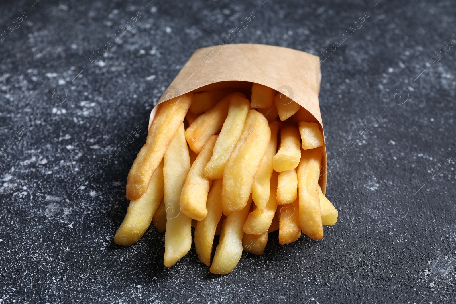 Photo of Delicious french fries in paper box on black textured table, closeup