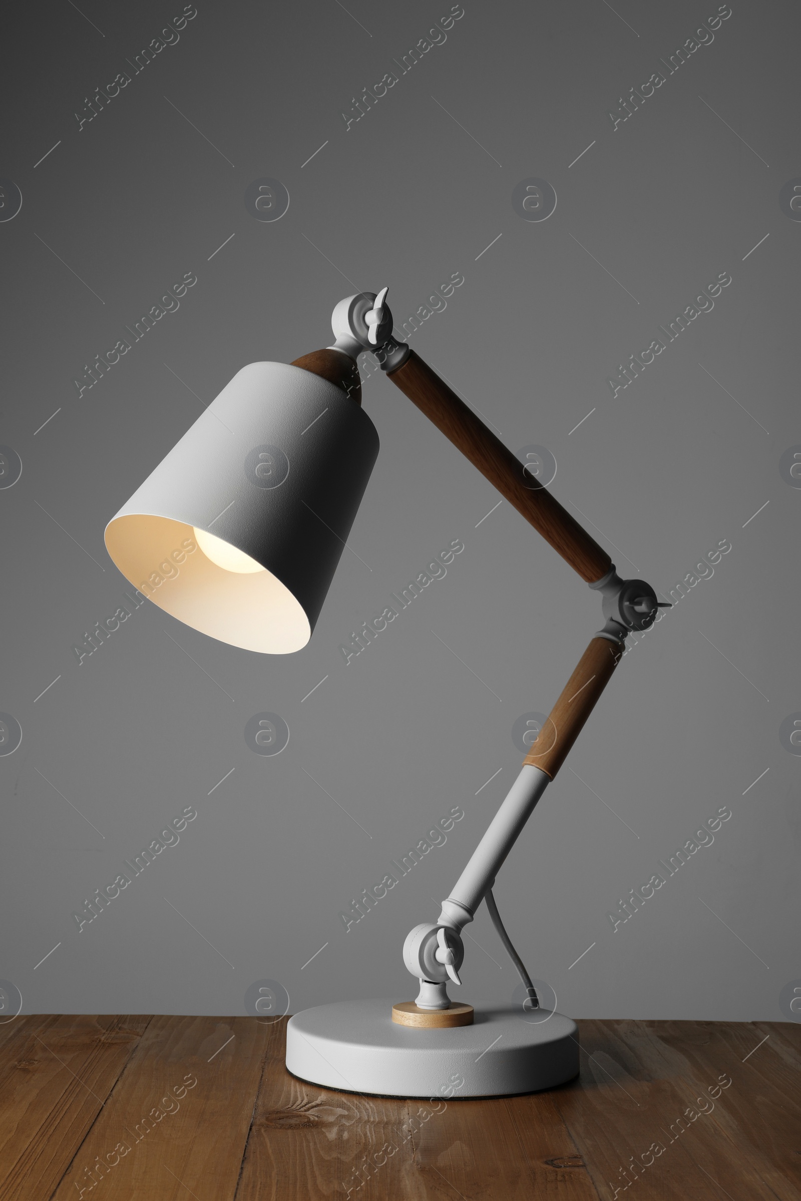 Stylish modern desk lamp on wooden table against grey background Photo of Stylish modern desk lamp on wooden table against grey background