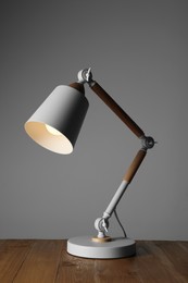 Photo of Stylish modern desk lamp on wooden table against grey background