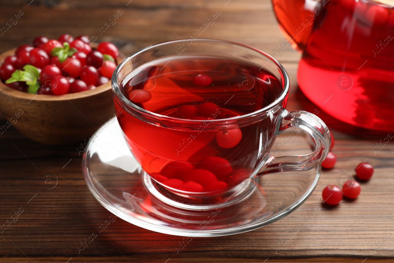 Photo of Tasty hot cranberry tea in glass cup and fresh berries on wooden table