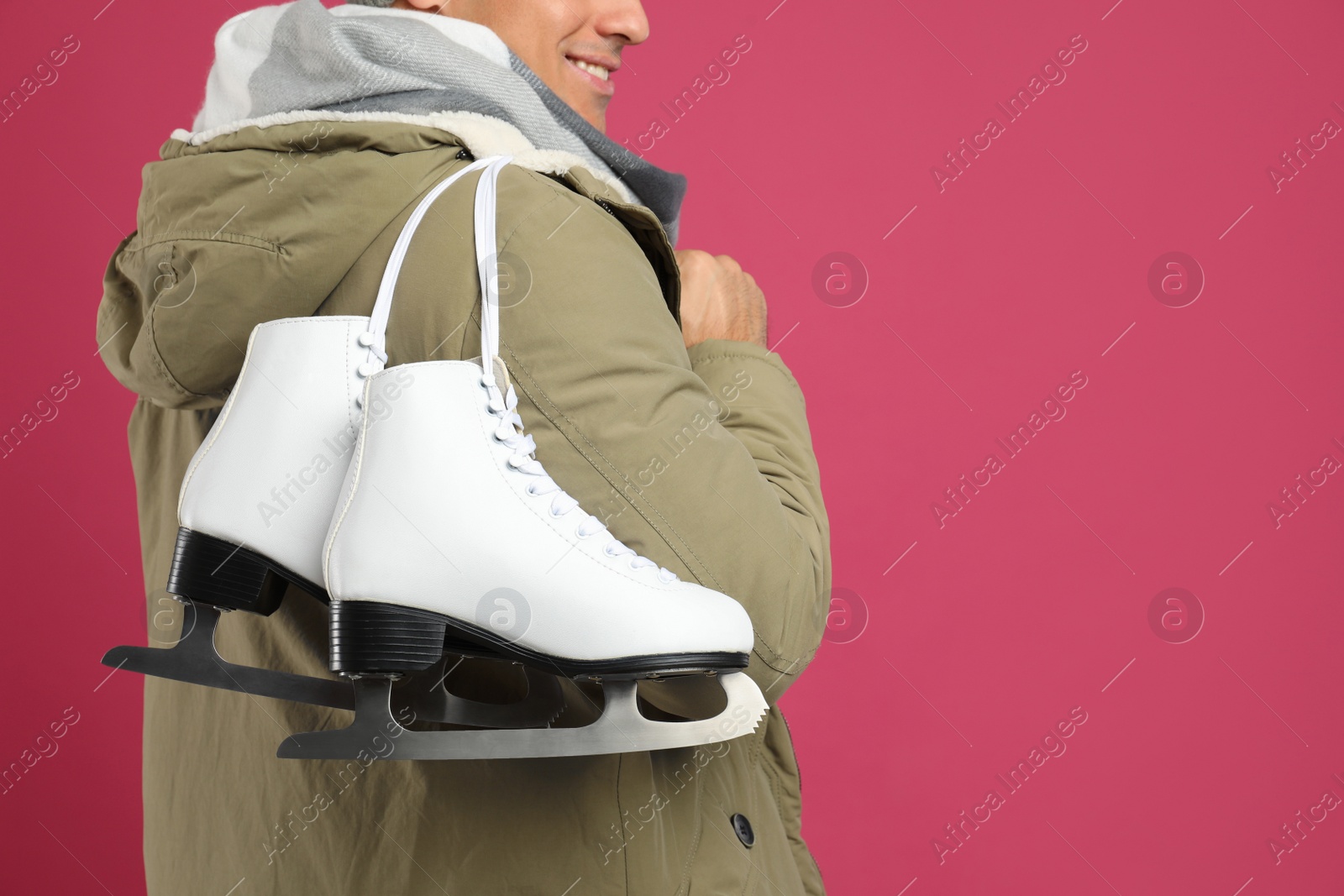 Photo of Happy man with ice skates on pink background, closeup. Space for text