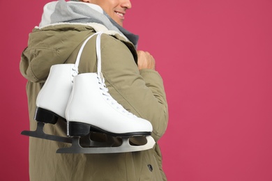 Photo of Happy man with ice skates on pink background, closeup. Space for text