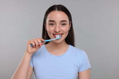Photo of Happy young woman brushing her teeth with plastic toothbrush on light grey background
