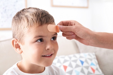 Photo of Woman applying adhesive bandage on boy's forehead indoors