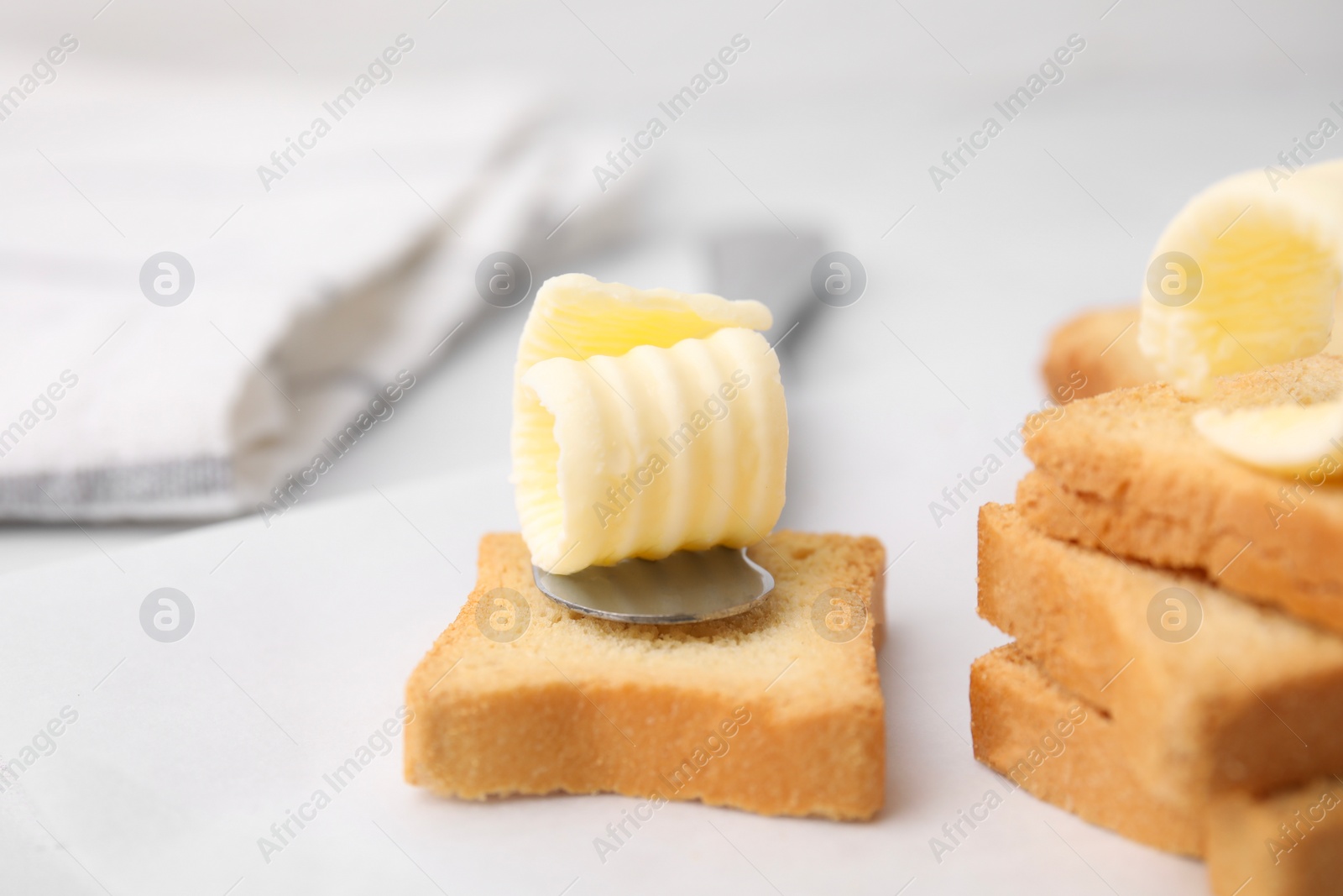 Photo of Tasty butter curls, knife and pieces of dry bread on white table, closeup