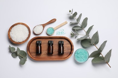 Photo of Aromatherapy products. Bottles of essential oil, sea salt and eucalyptus leaves on white background, flat lay