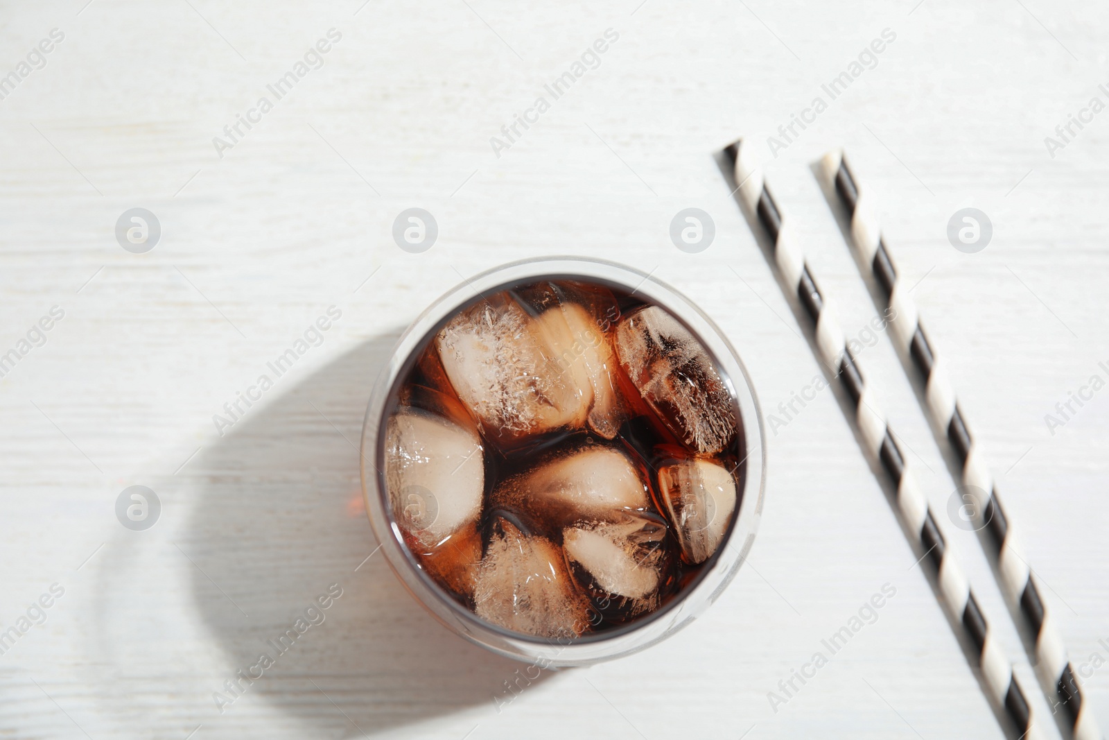 Photo of Glass of refreshing cola with ice cubes on white wooden background, top view