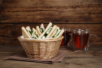 Photo of Tasty sandwiches with cucumber and parsley in wicker basket on wooden table