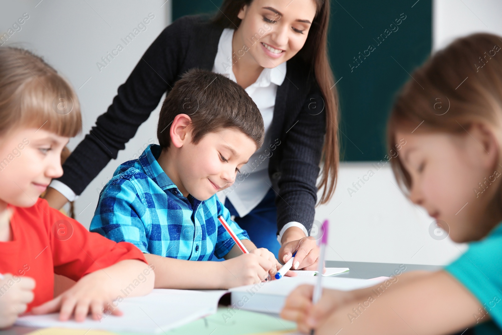 Photo of Female teacher helping boy with his task in classroom at school