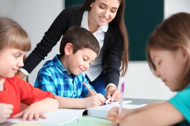 Photo of Female teacher helping boy with his task in classroom at school