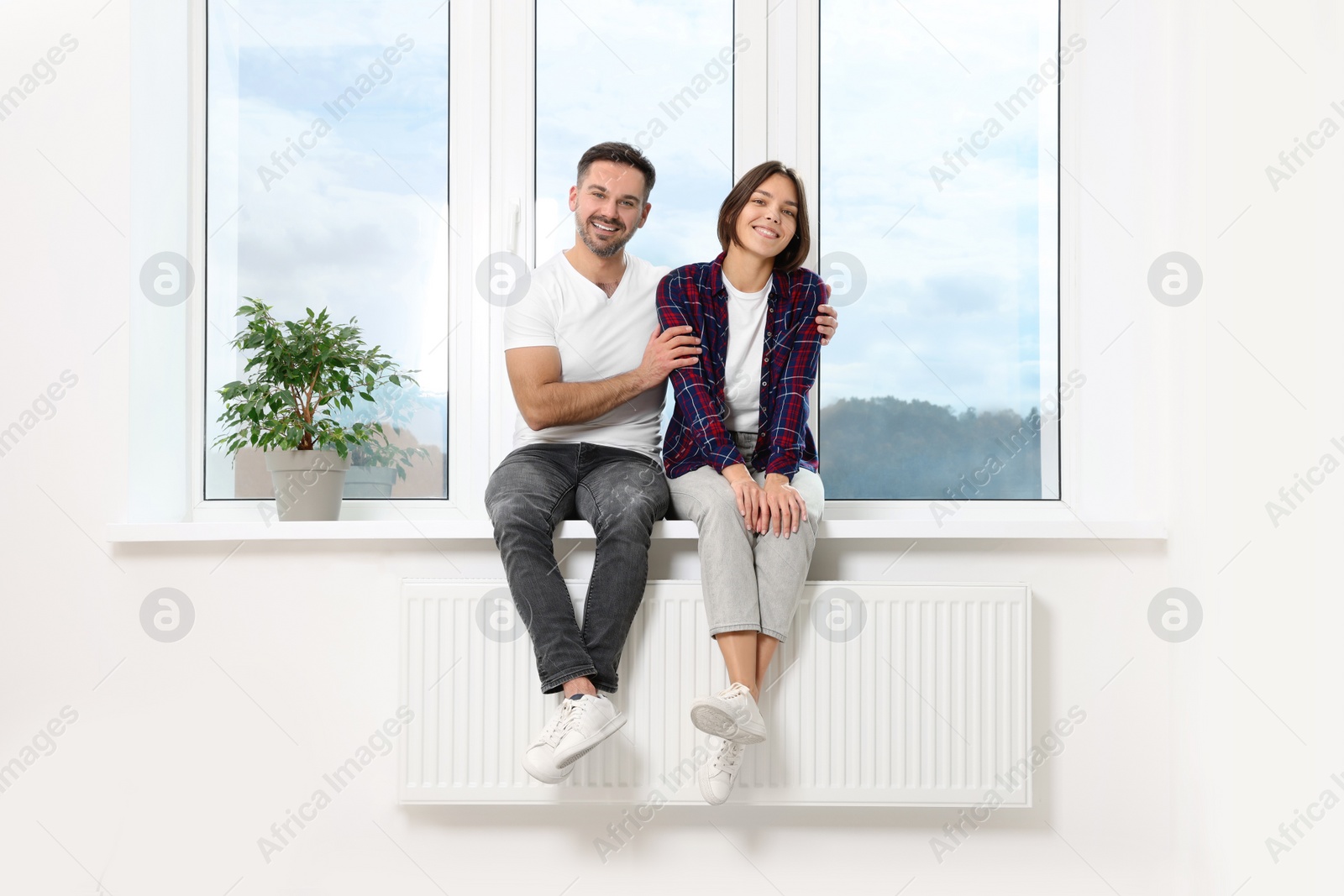 Photo of Happy couple sitting on windowsill in new apartment. Moving day