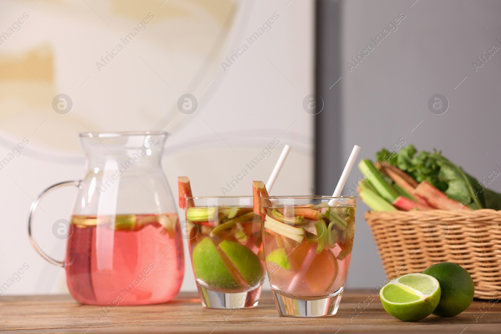 Photo of Glasses and jug of tasty rhubarb cocktail with lime fruits on wooden table