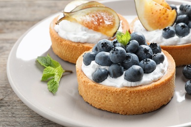 Photo of Plate of tarts with blueberries and figs on wooden table, closeup. Delicious pastries