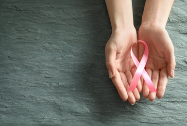 Woman holding pink ribbon on grey stone background, top view with space for text. Breast cancer awareness