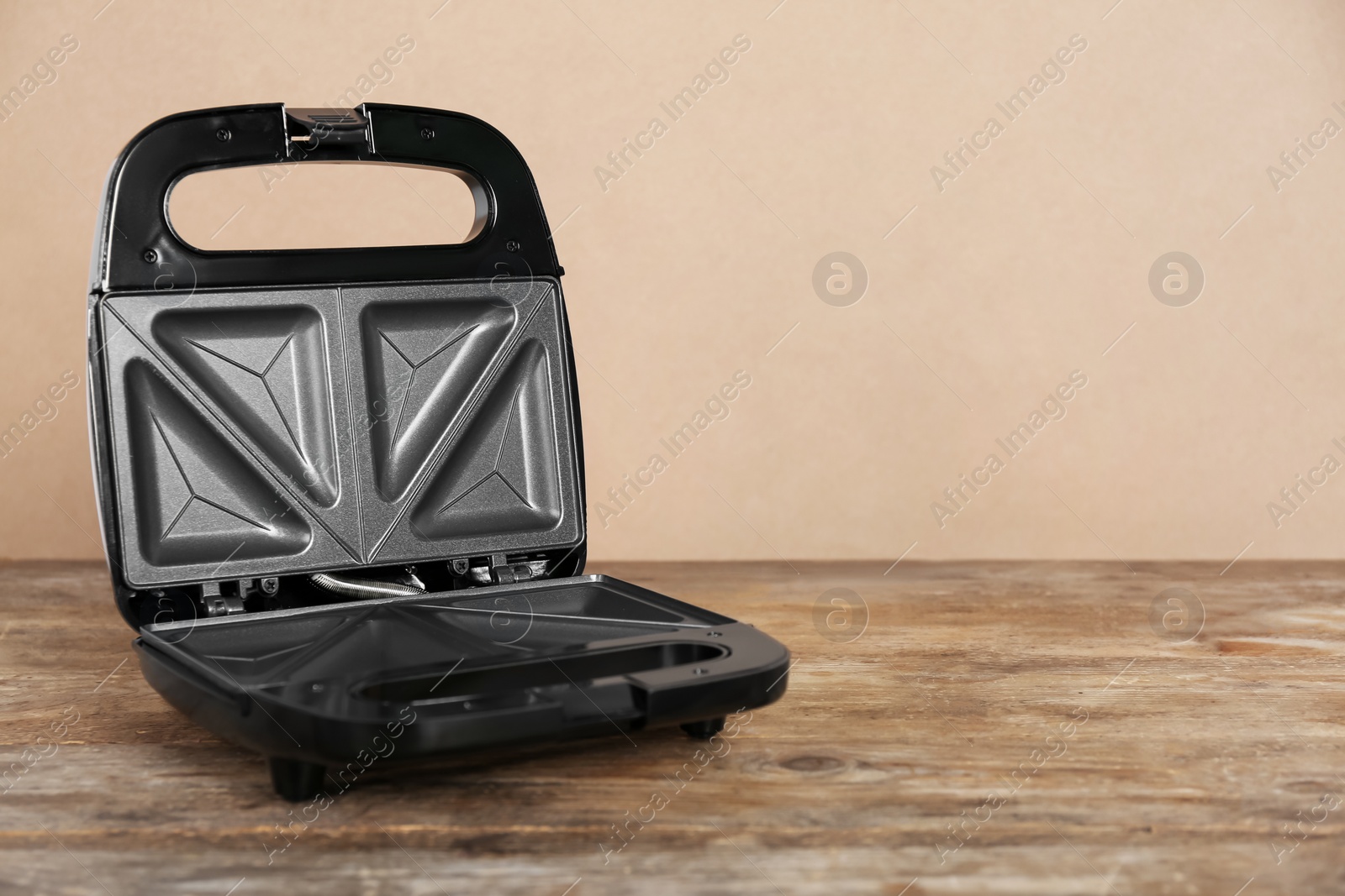 Photo of Open electric sandwich maker on wooden table against beige background, space for text