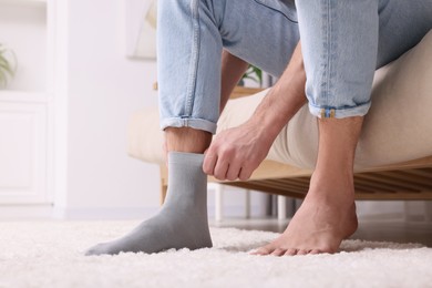 Man putting on grey sock at home, closeup. Space for text