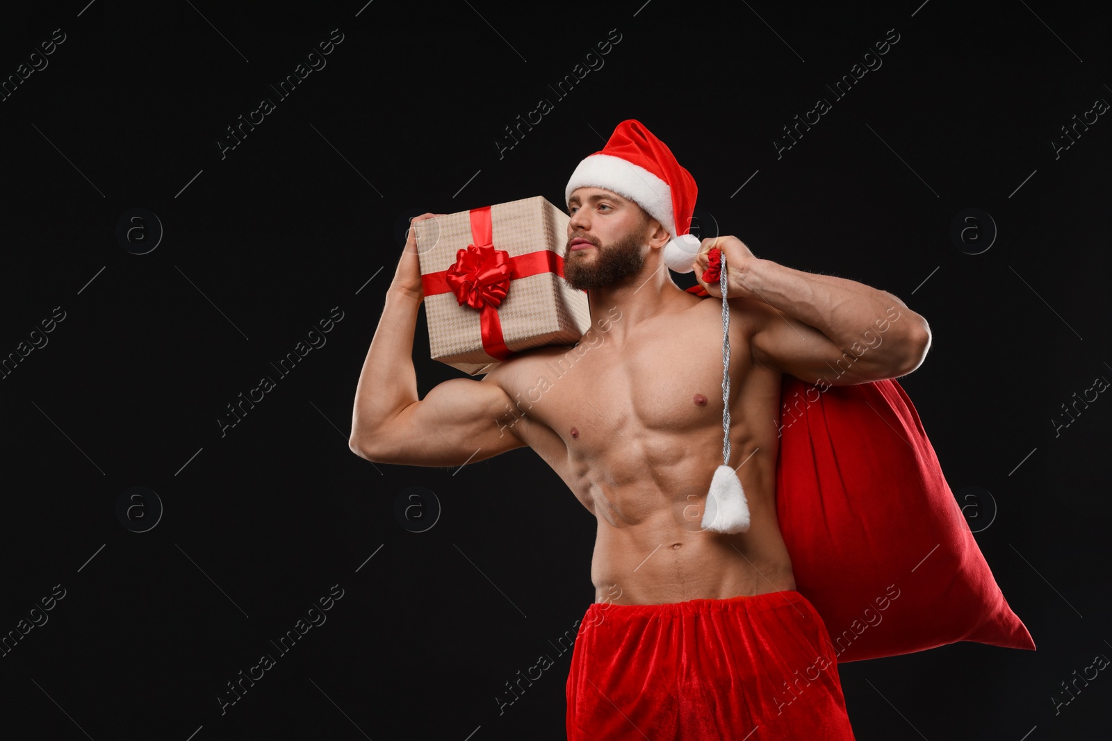 Photo of Attractive young man with muscular body holding bag and Christmas gift box on black background, space for text