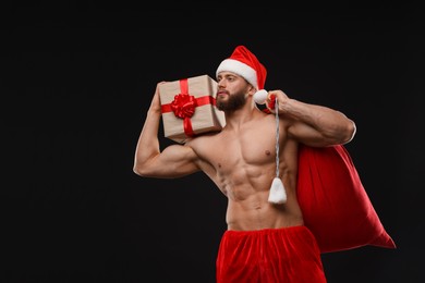 Photo of Attractive young man with muscular body holding bag and Christmas gift box on black background, space for text